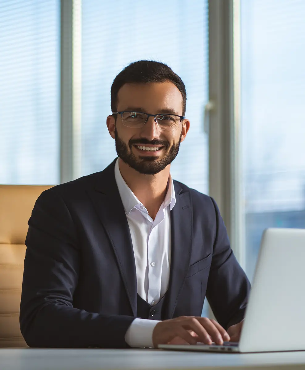 Happy man with glasses working on a laptop at his desk, smiling while giving feedback reflecting satisfaction with our services.