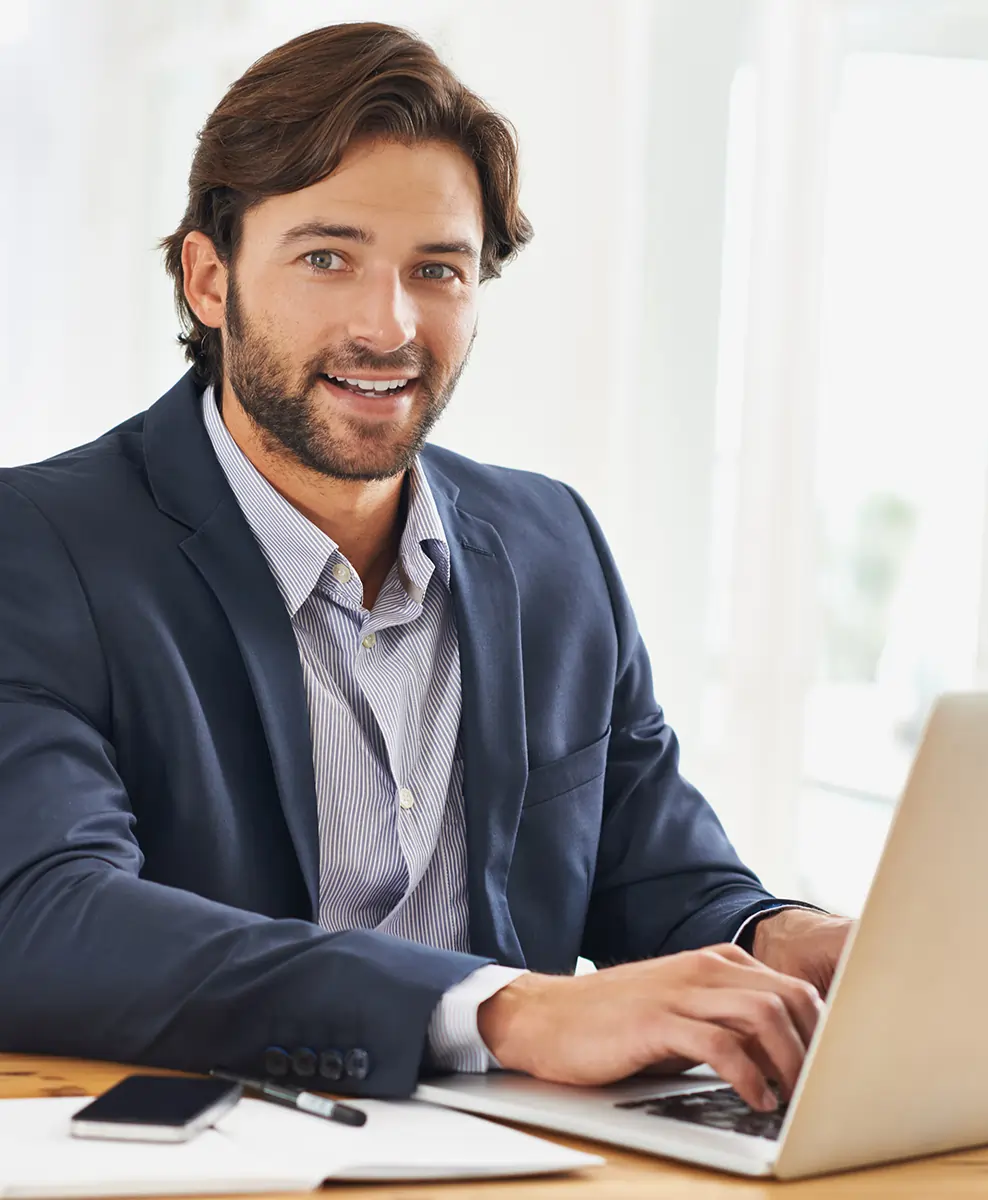 Happy man with glasses working on a laptop at his desk, smiling while giving feedback reflecting satisfaction with our services.